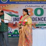 Woman in a peach saree holding a flower bouquet standing on a stage in front of an indian independence celebration banner